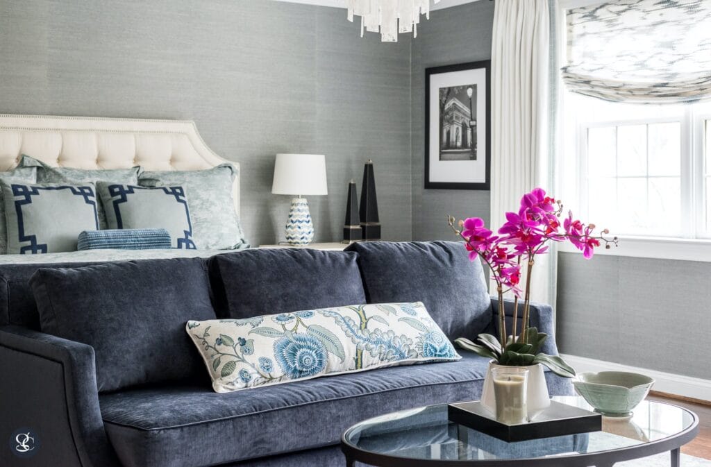 A grey sofa with a floral throw pillow and purple orchid