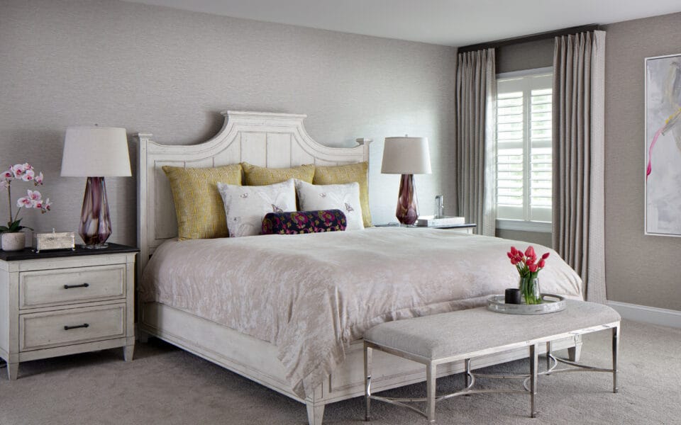 A master bedroom with neutral bedding and floor length window treatments